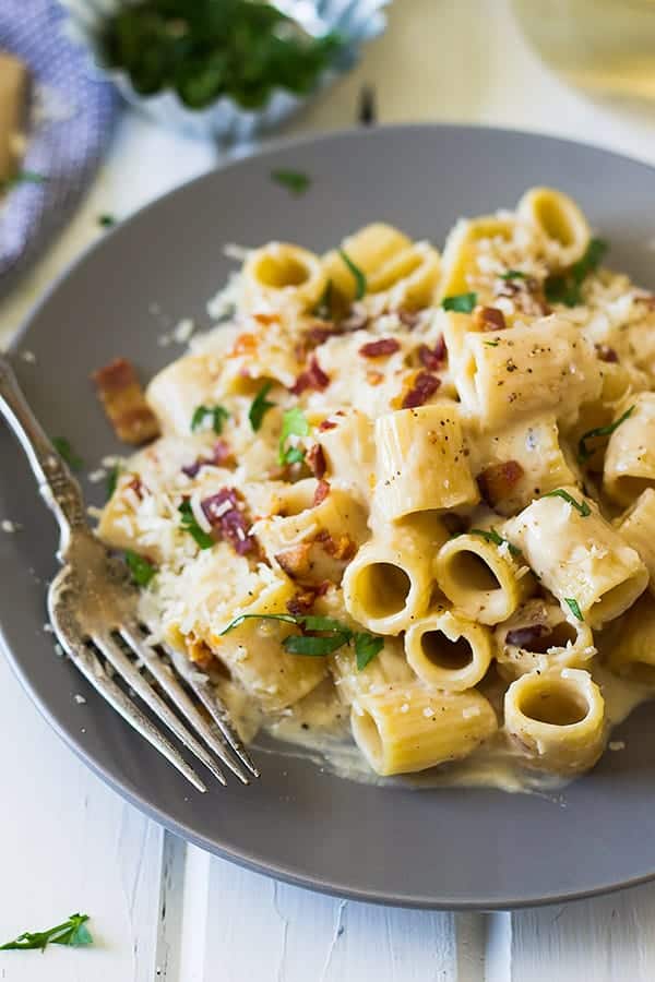 a plate of alfredo pasta with bacon and a fork