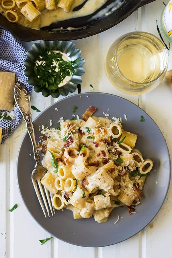 overhead: a plate of bacon alfredo pasta with a glass of white wine