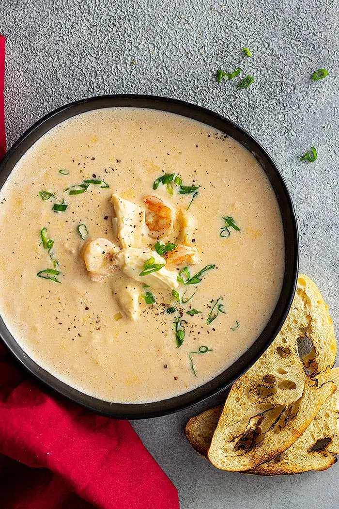 overhead: crab and shrimp seafood bisque in a black bowl garnished with green onions and black pepper