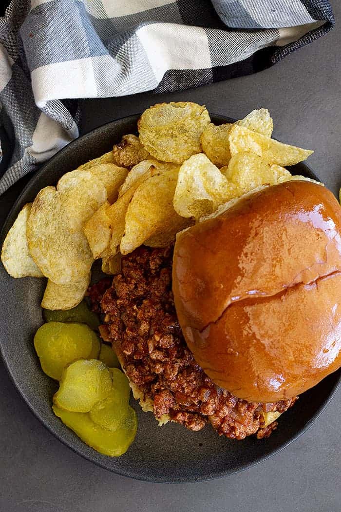 overhead: homemade sloppy joe mix on a hamburger bun with sliced pickles and potato chips on the side