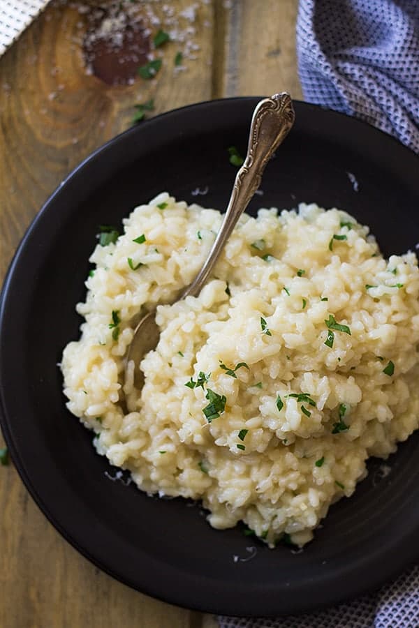overhead: parmesan risotto recipe garnished with fresh chopped parsley on a black plate with a fork