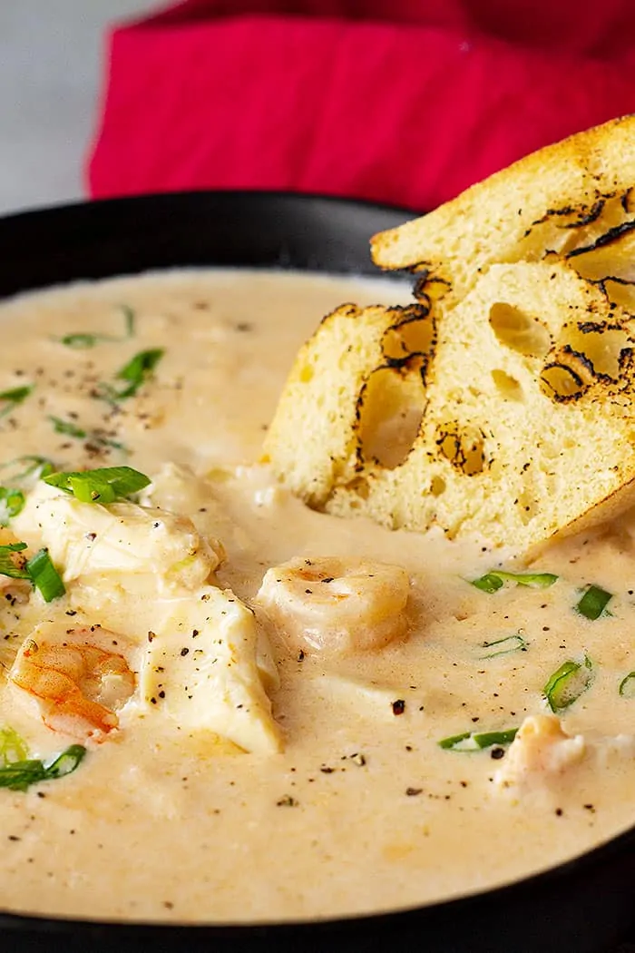 closeup: seafood bisque in a bowl with a piece of crusty bread dipping into it