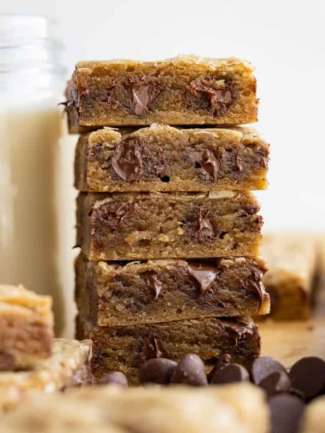Tall stack of chocolate chip cookie bars next to a tall glass of milk.