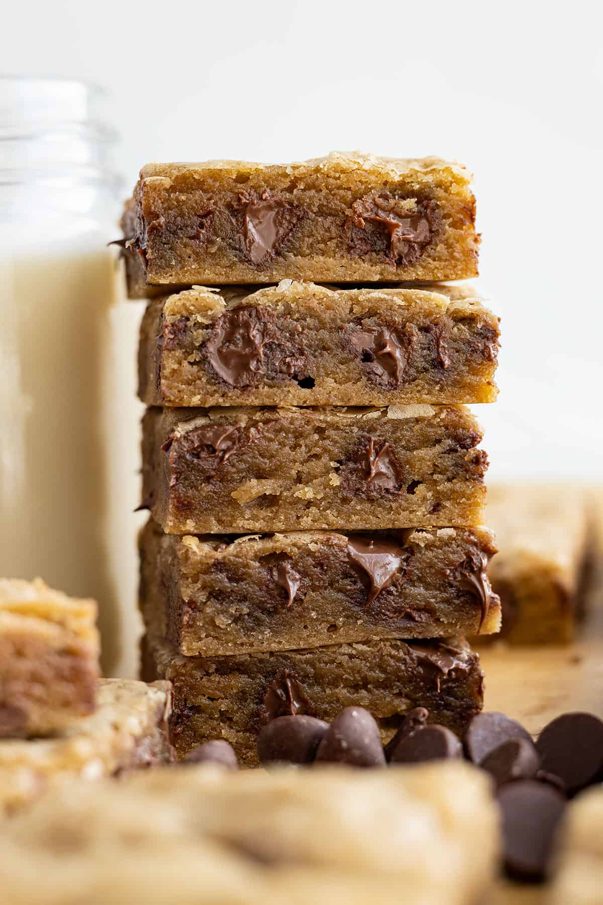 Tall stack of chocolate chip cookie bars next to a tall glass of milk.