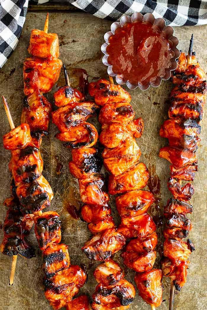 overhead: BBQ chicken kabobs on a baking sheet with homemade BBQ sauce to the side