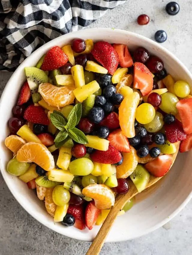 Overhead view of easy fruit salad in a cream bowl with a spoon in the salad. Garnished with mint.