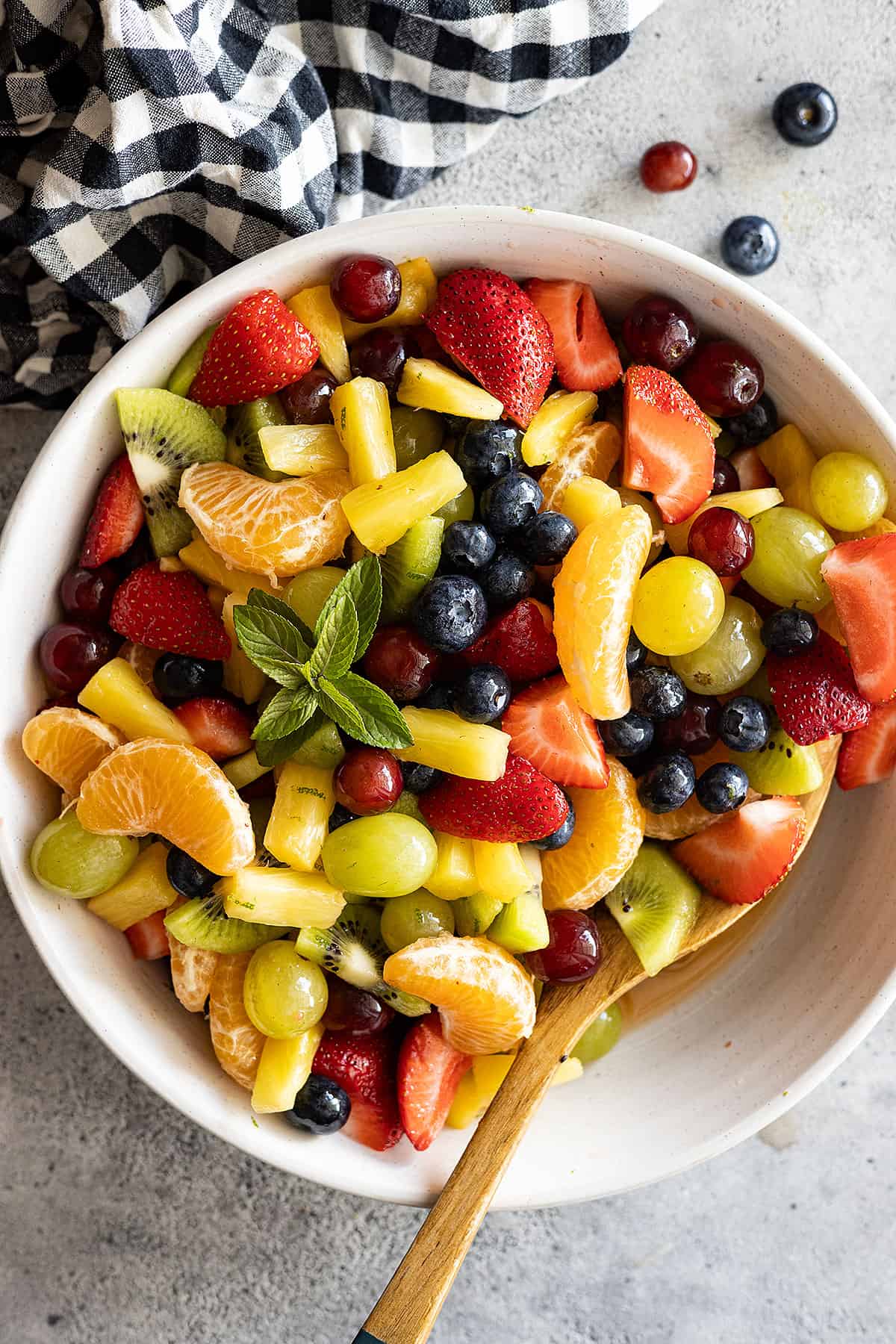 Overhead view of easy fruit salad in a cream bowl with a spoon in the salad. Garnished with mint. 