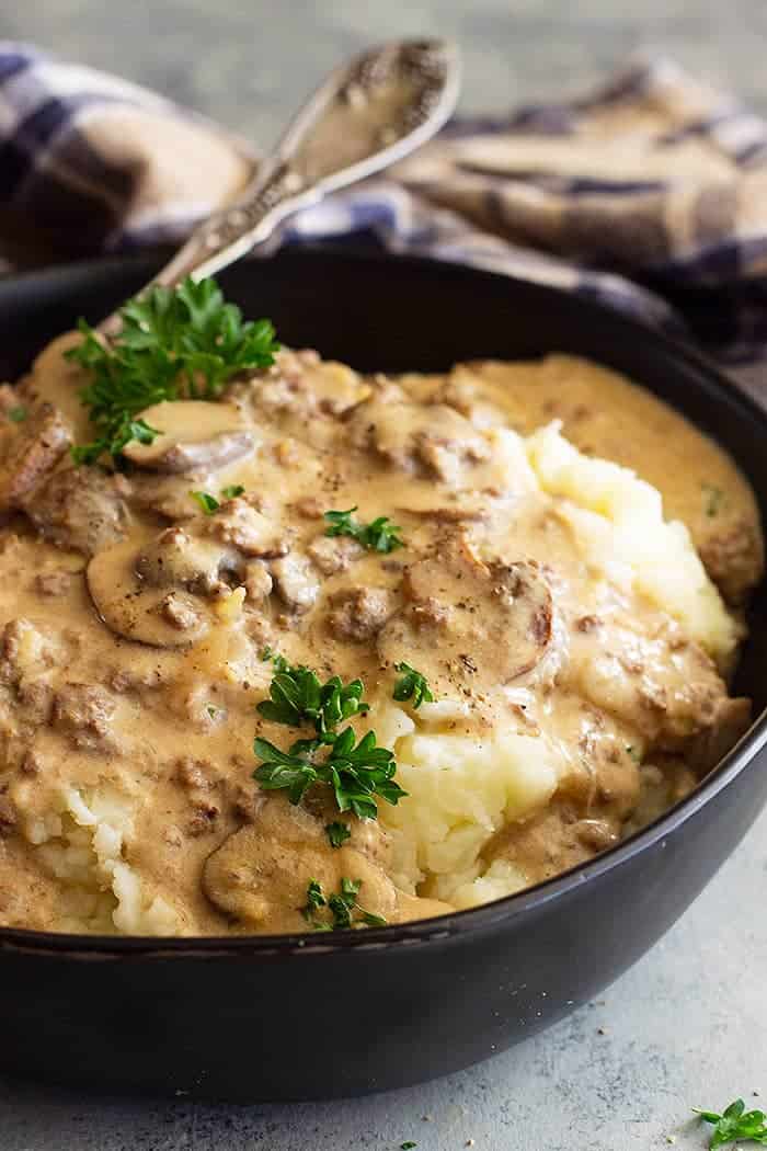 closeup: saucy hamburger beef stroganoff recipe over mashed potatoes with fresh herbs on top