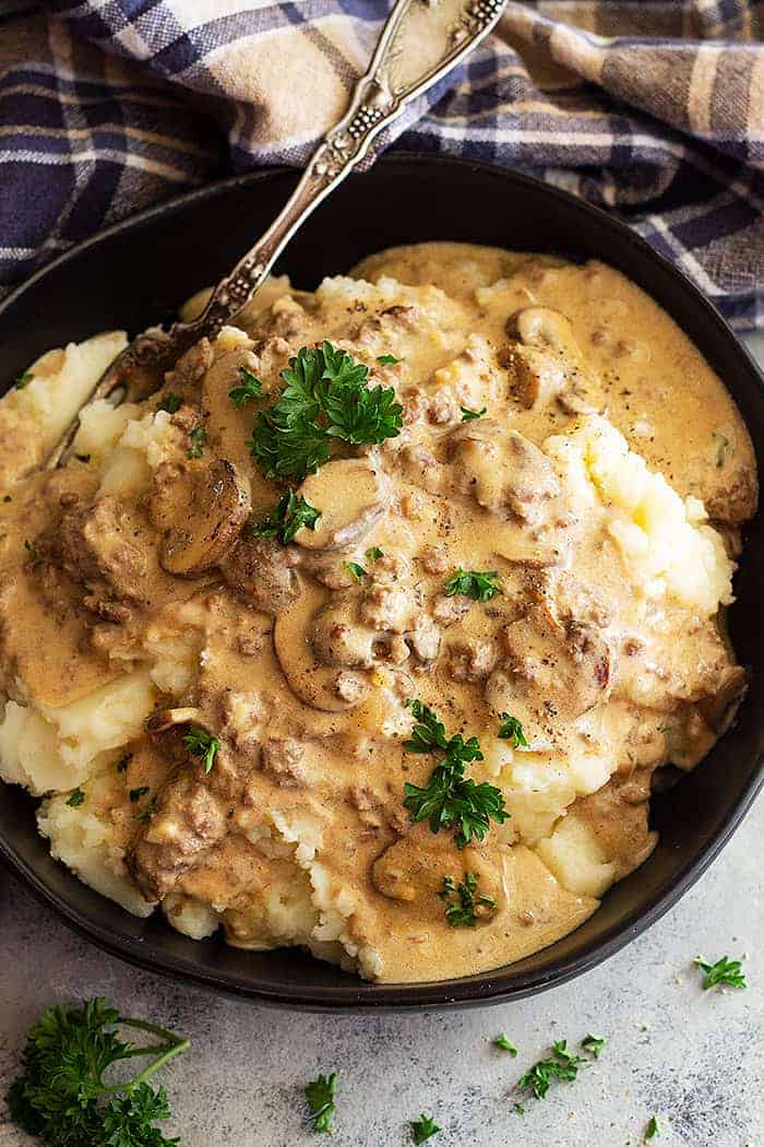 overhead closeup: hamburger stroganoff recipe over mashed potatoes in a black bowl