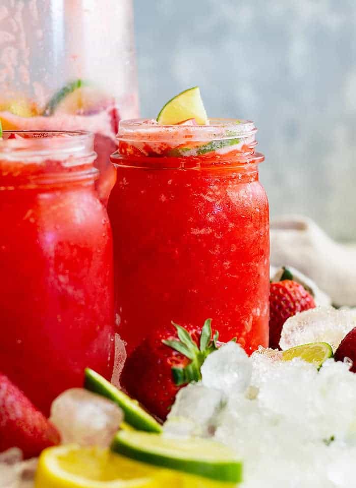 two glasses of strawberry lemonade with ice, fresh strawberries, and lime slices
