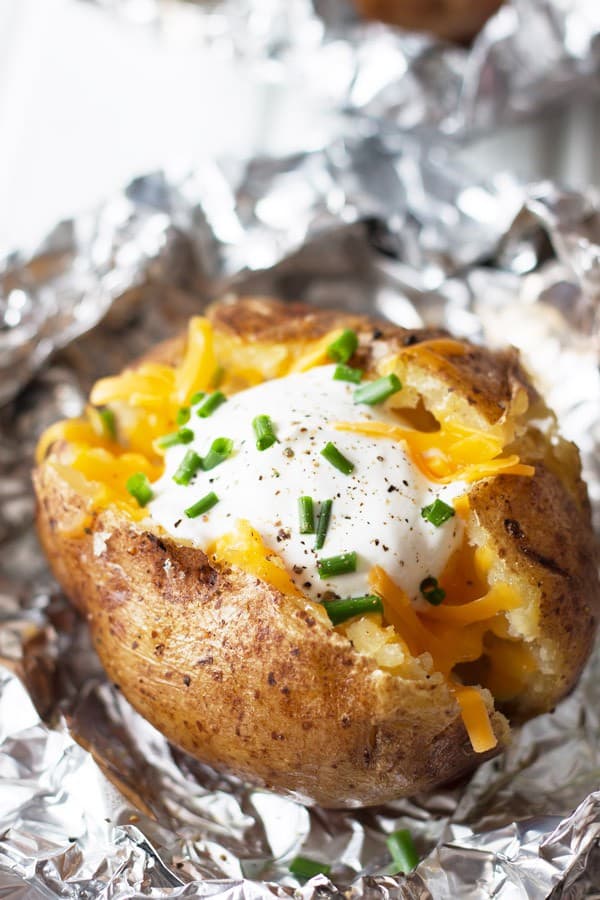 closeup: baked potato split open and dressed with sour cream and colby jack cheese 