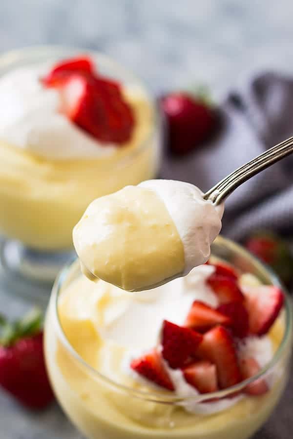 closeup: a spoonful of homemade vanilla pudding with whipped cream over a bowl with more