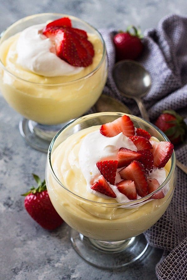 overhead: 2 bowls of vanilla pudding from scratch topped with whipped cream and fresh strawberries