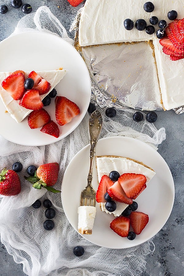 overhead: slices of no bake vanilla cheesecake with berries on plates next to whole cheesecake