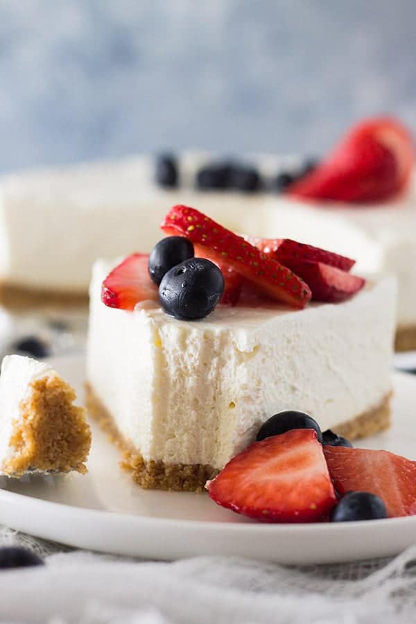 front view: a slice of no bake vanilla cheesecake recipe with a forkful removed. Fresh berries top the cheesecake
