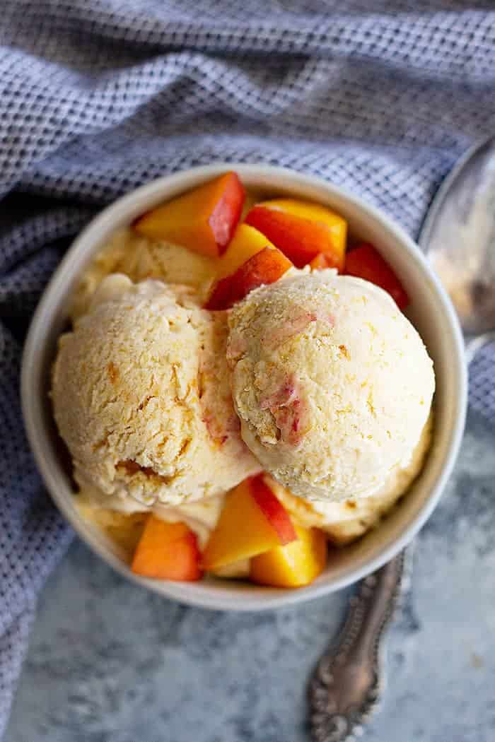 overhead: no churn peach ice cream in a bowl with extra fresh peaches