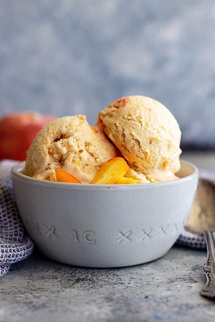 side view closeup: a bowl of peach ice cream recipe topped with fresh peaches