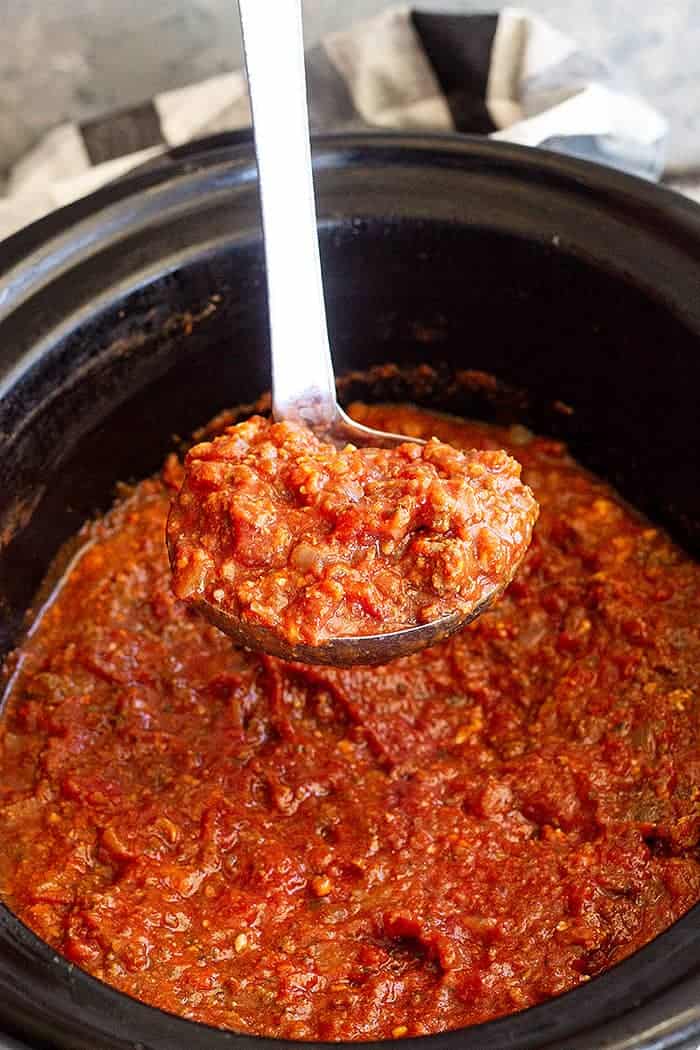 overhead closeup: scooping out a ladle of sauce over spaghetti sauce in crock pot