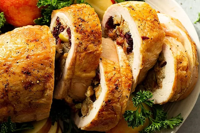 overhead closeup: several slices of stuffed turkey breast garnished with cut apples, parsley, and dried cranberries on the serving plate