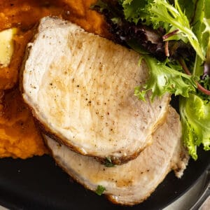 Overhead of sliced pork on a black plate with mashed sweet potatoes and a salad.
