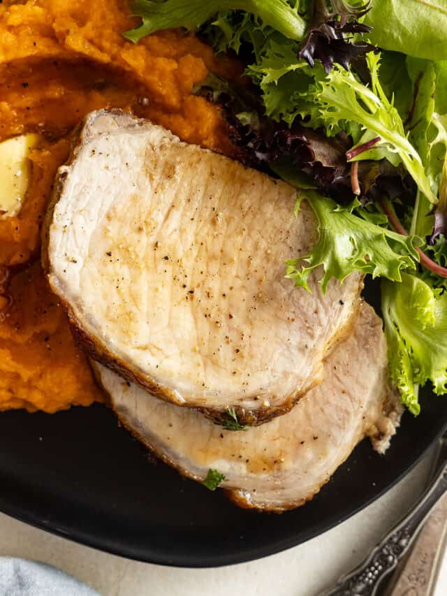 Overhead of sliced pork on a black plate with mashed sweet potatoes and a salad.