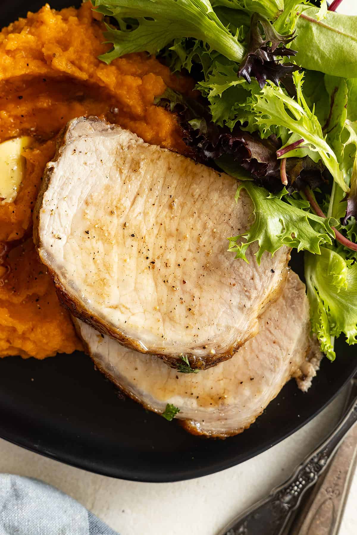 Overhead of sliced pork on a black plate with mashed sweet potatoes and a salad. 