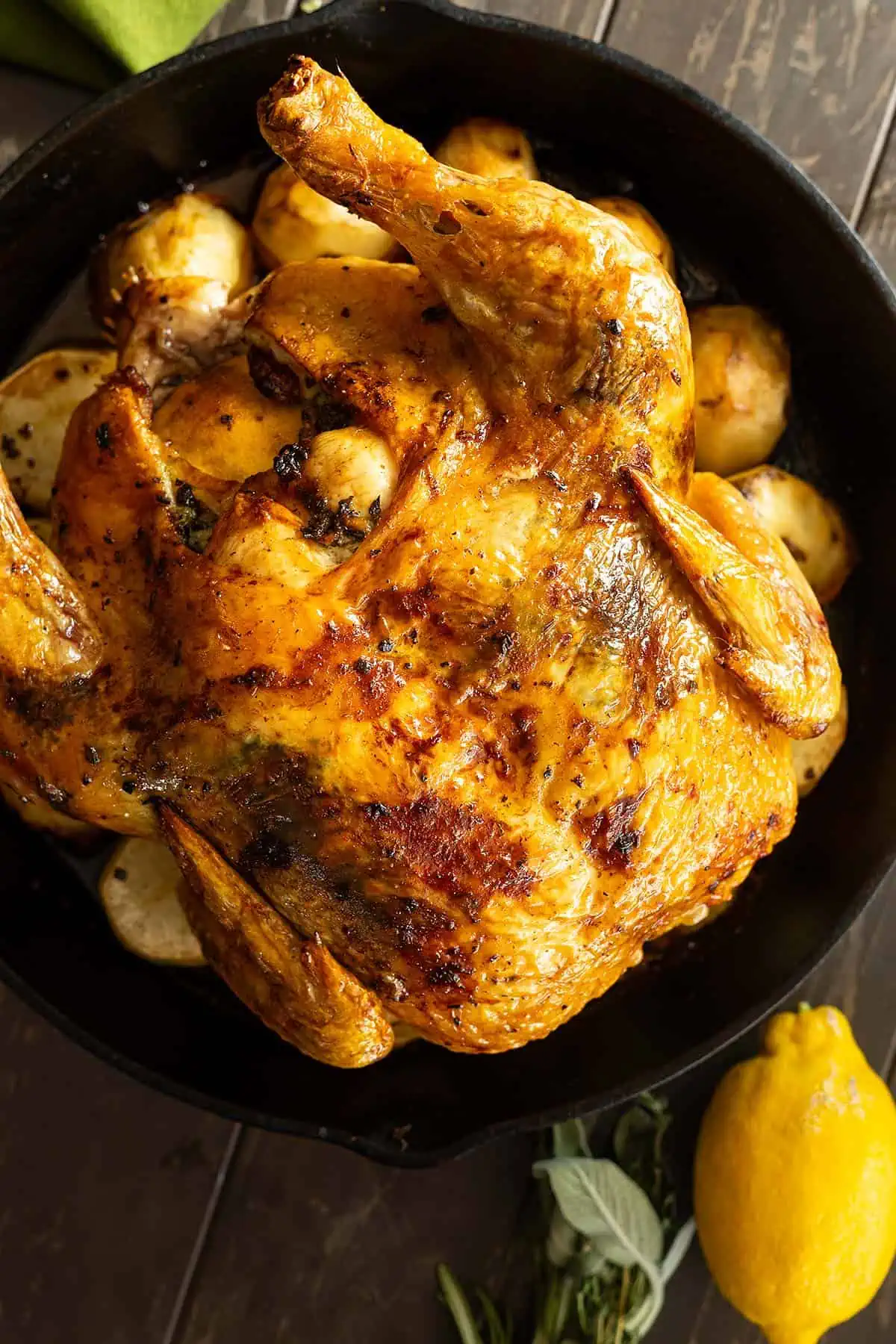 Overhead view of roasted chicken fresh from the oven. Lemon and fresh herbs off to the side.