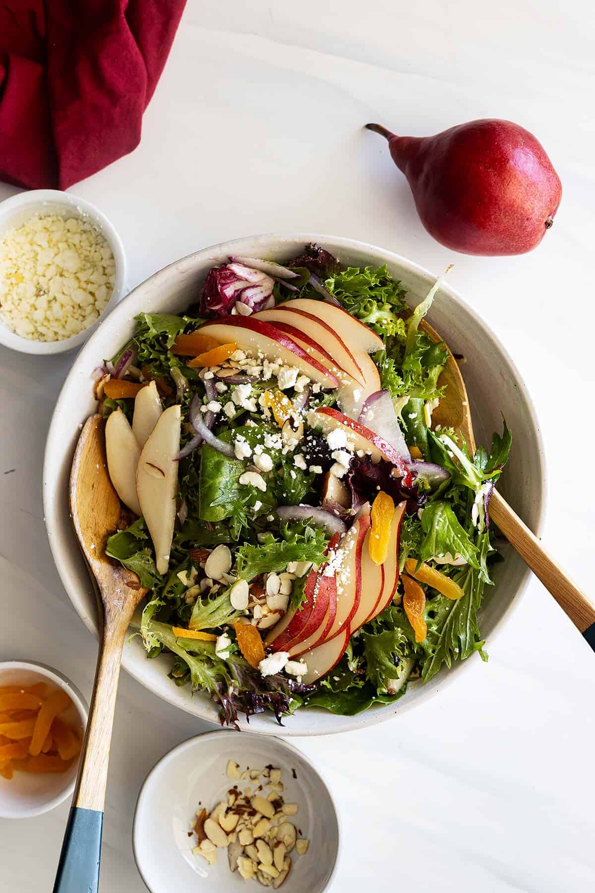 Overhead view of salad in a large white bowl. Sliced pear fanned out in different spots. Small bowls of ingredients used in salad off to the side. 