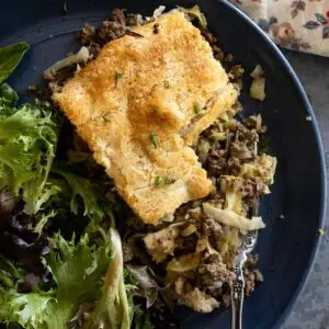 Overhead view of runza casserole with bite taken out showing the contents of the casserole. Salad off to the side of the plate.