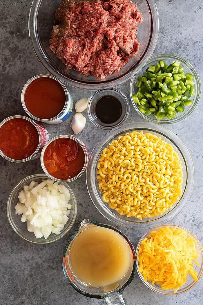 overhead: ingredients needed to make this American goulash recipe: elbow noodles, ground beef, canned tomatoes