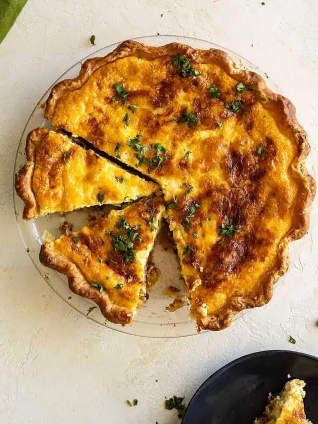 Overhead view of quiche in pie plate with slices cut and one removed and on a plate in the corner.