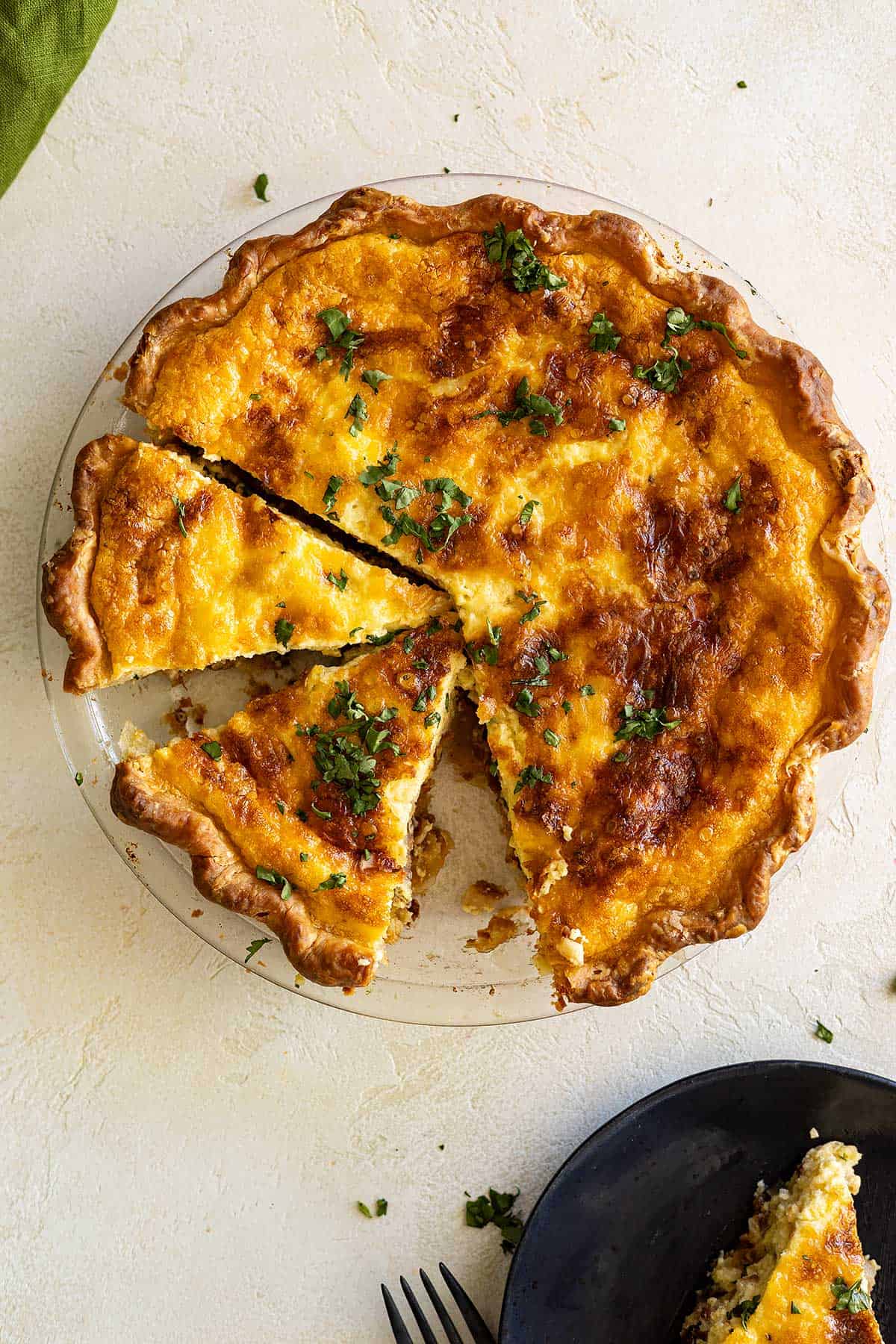 Overhead view of quiche in pie plate with slices cut and one removed and on a plate in the corner. 