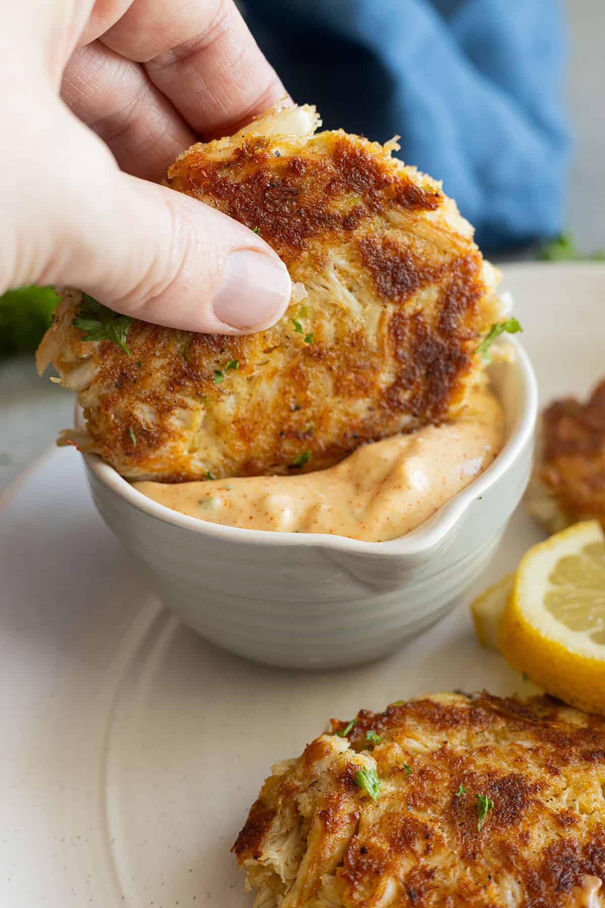 A crab cake being dipped into the remoulade sauce. 