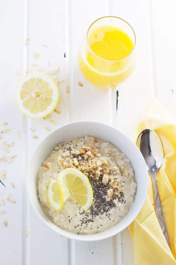overhead: a bowl of overnight cheesecake oats on a table with oats and lemons