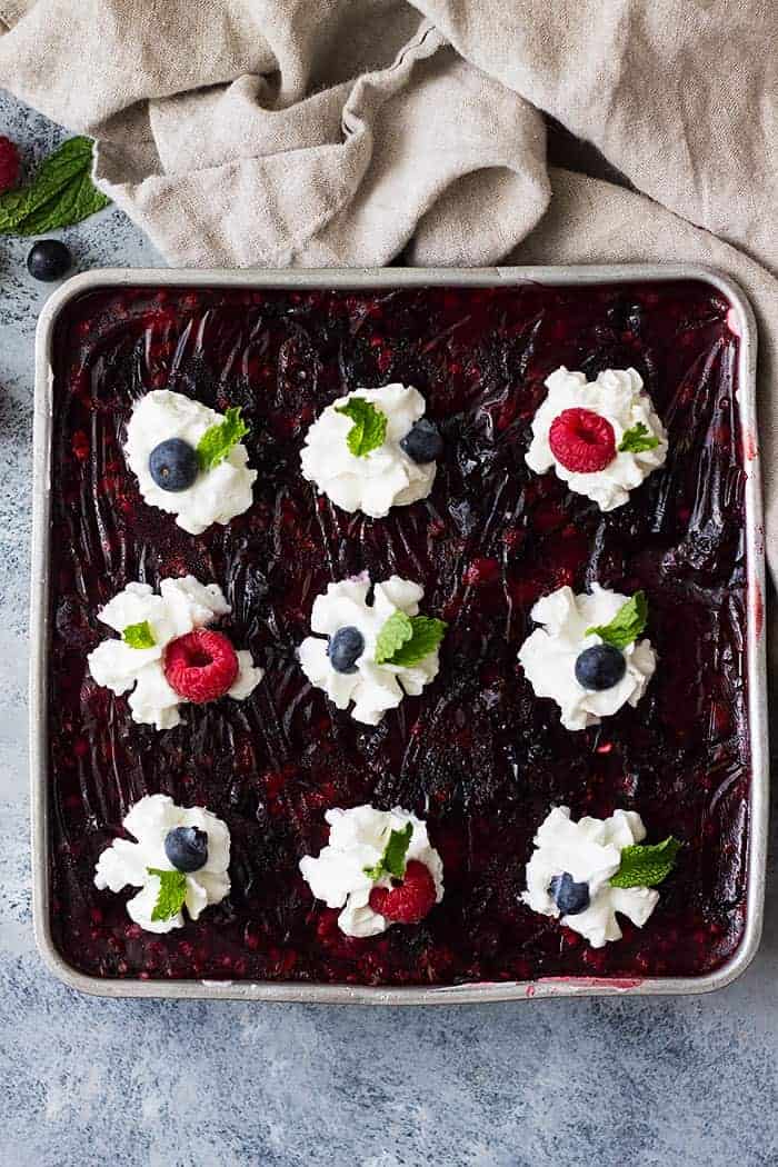 overhead: full baking pan of raspberry pretzel jello salad with whipped cream and mixed berries on top
