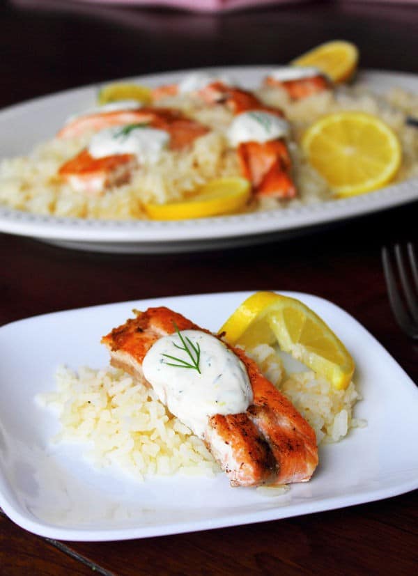 salmon and lemon rice with dill sauce on top on a white plate 