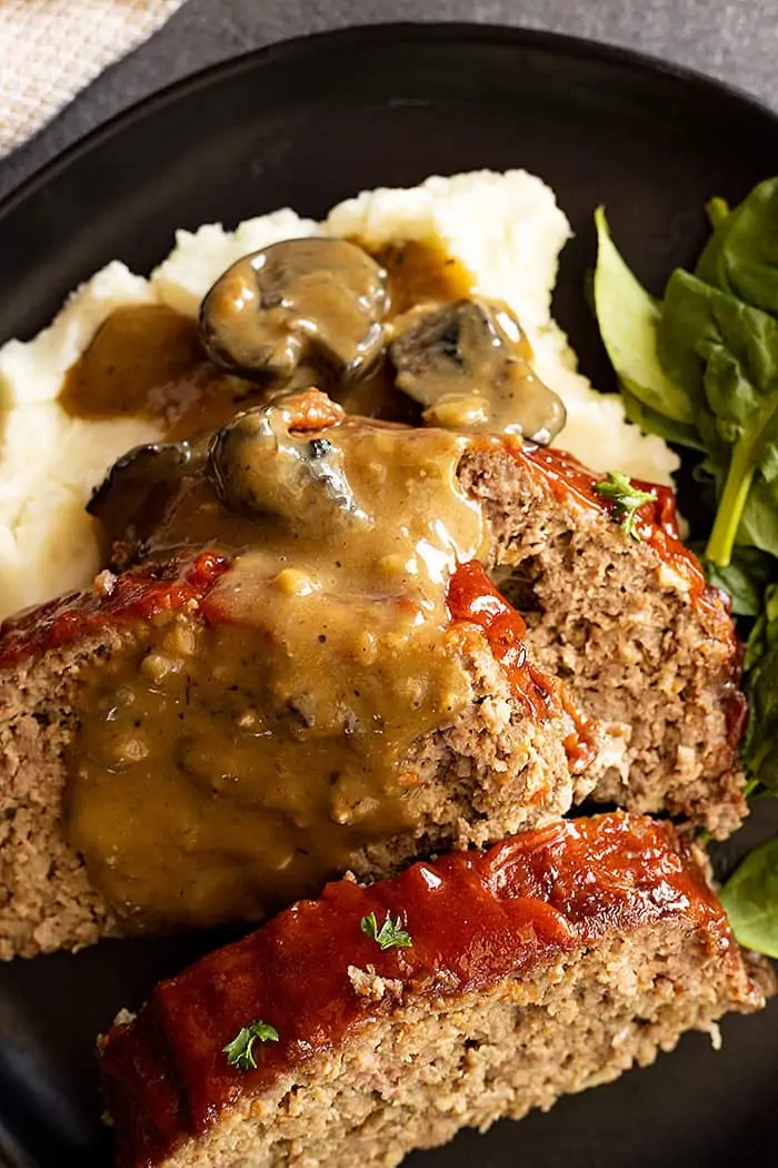 closeup: mushroom gravy spooned over 3 slices of easy meatloaf recipe with oats and mashed potatoes