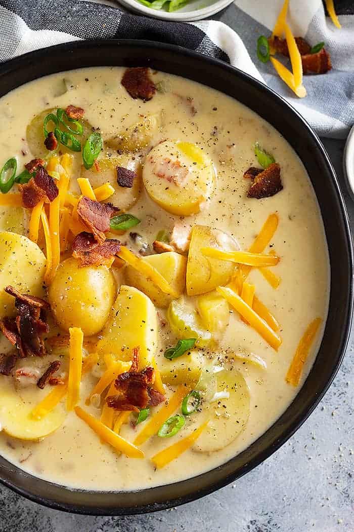 overhead: a bowl of easy potato soup recipe on stovetop with potatoes, bacon, cheddar cheese, and green onions