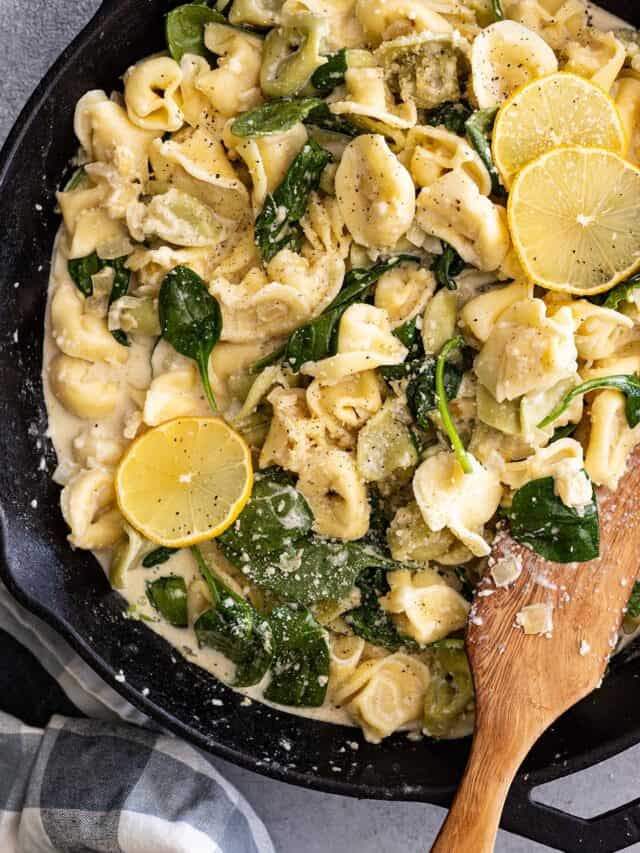 Overhead view of creamy lemon tortellini in a skillet with wood spatula to the side.