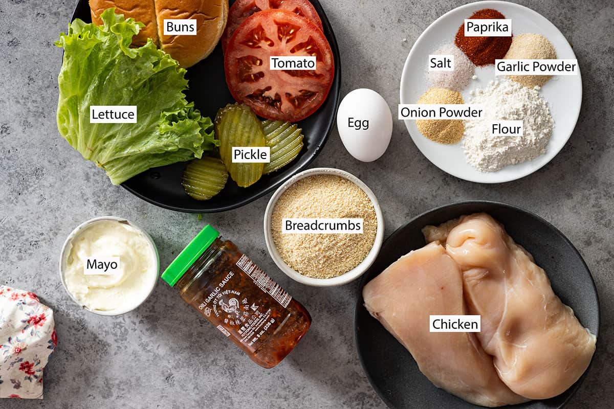 Ingredients: chicken, mayo, chili sauce, paprika, garlic powder, onion powder, salt, flour, breadcrumbs, egg, lettuce, buns, tomato, and pickles. 