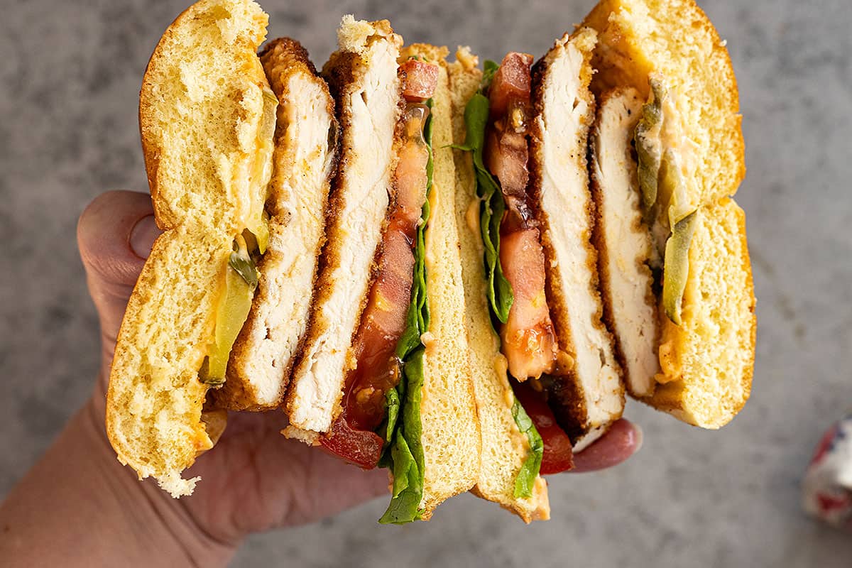 Hand holding sandwich cut in half showing all the delicious layers.