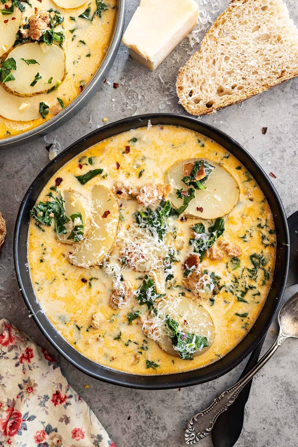 Overhead view of a bowl of soup. A chunk of parmesan off to the side along with slices of bread.