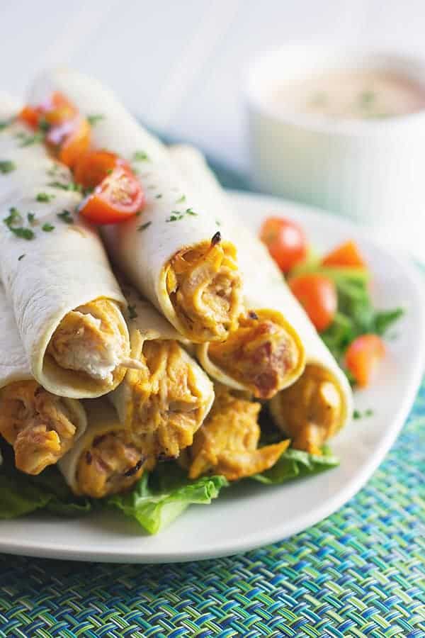 closeup: my chicken taquito recipe on a white serving plate with chopped tomatoes and fresh cilantro