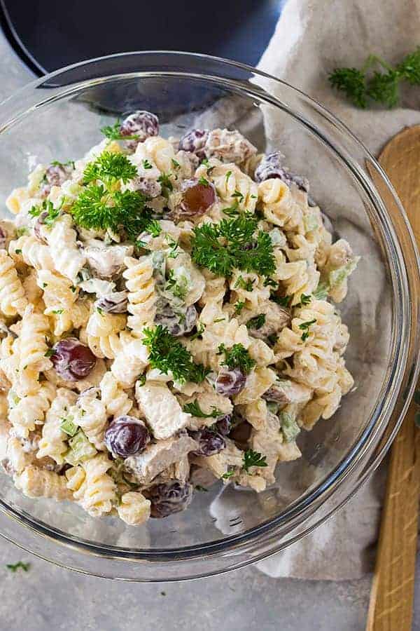 overhead: large bowl of chicken and pasta salad with mayo and red grapes in clear glass mixing bowl