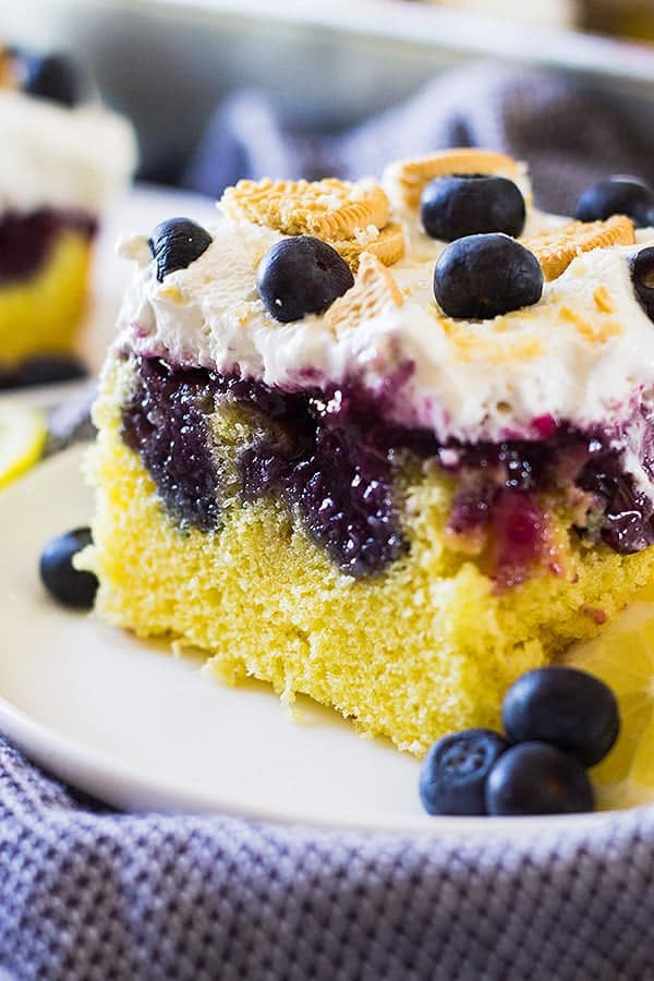 closeup: a slice of lemon blueberry poke cake on a plate with all of the layers and toppings showing