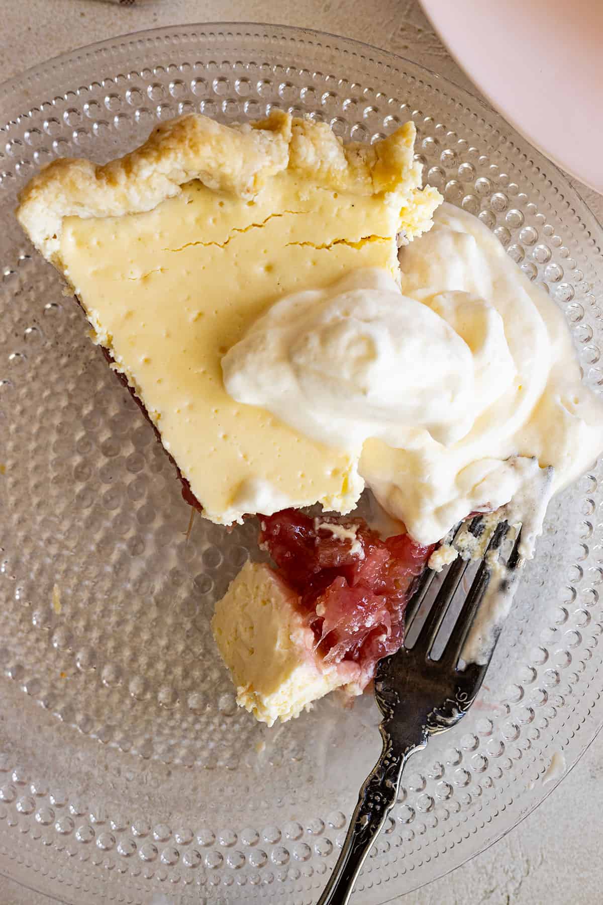 Overhead view of a piece of pie on a glass plate topped with whipped cream and a bite being taken out. 