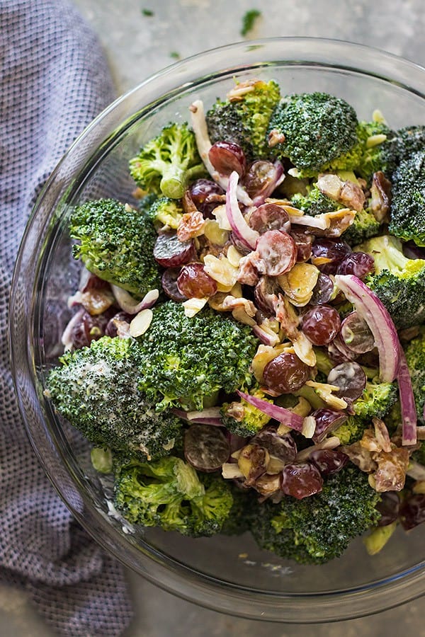 overhead closeup: a large bowl of broccoli grape salad with red onion, nuts, and bacon on top