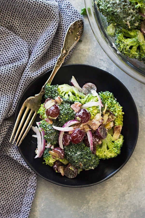 overhead: a small black bowl of broccoli salad with grapes with a fork
