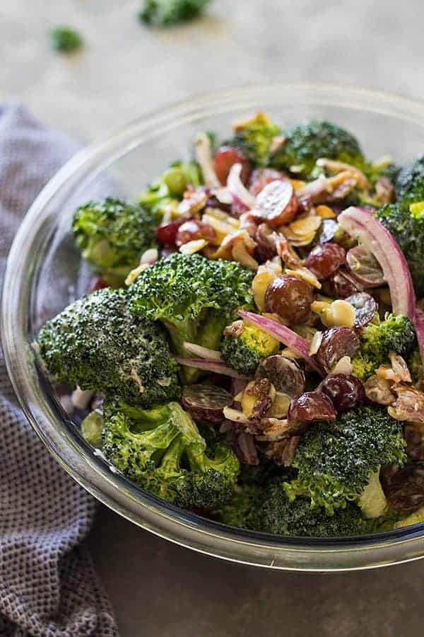 overhead: a large bowl of broccoli and grape salad with nuts and red onion on top