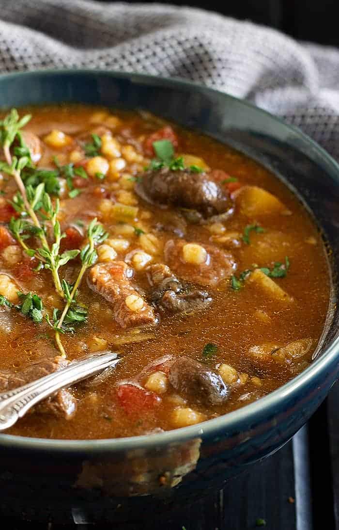 closeup: a bowl of comforting instant pot beef barley soup garnished with fresh thyme